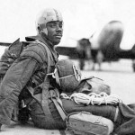 Historic photo of 555th Parachute Infantry Battalion soldier sitting on tarmac with aircraft in background